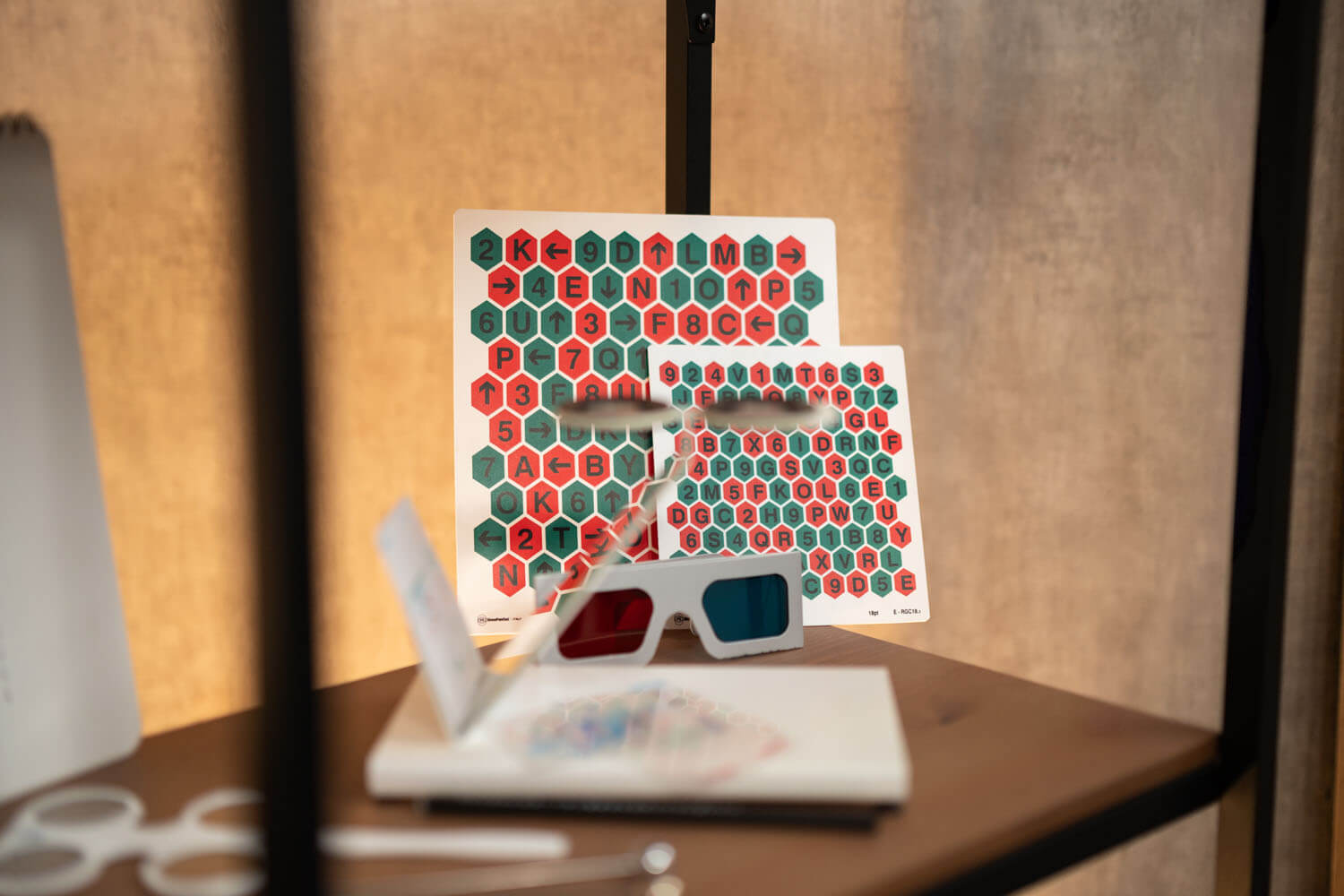 Karten mit Rot-Grün Hexagon-Muster und Zahlen und Buchstaben; davor leigt eine Rot/Blau-Brille